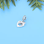 Silver heart-shaped pendant with a small figure inside on a blue background with green leaves.