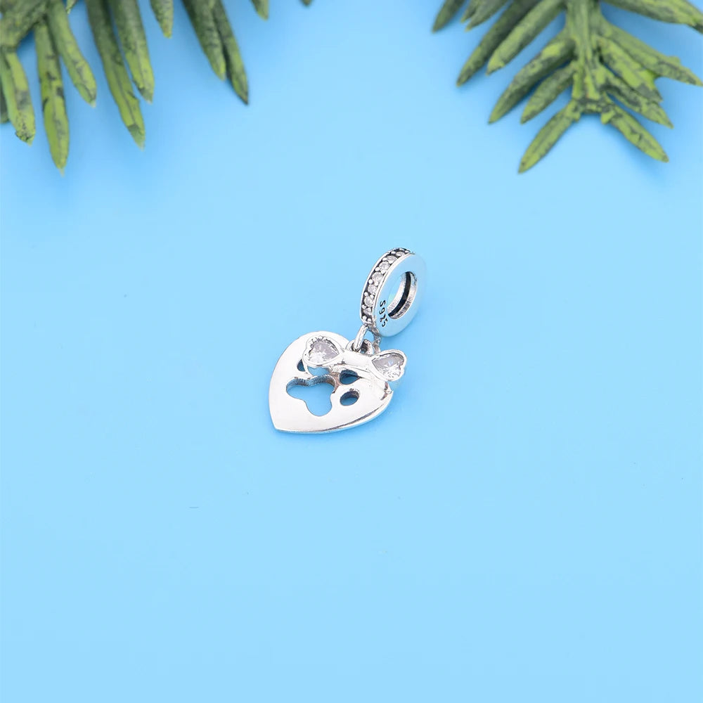Silver heart-shaped pendant with a small figure inside on a blue background with green leaves.