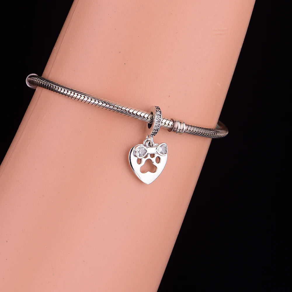 Silver bracelet with a heart-shaped charm featuring a paw print on a wrist against a black background